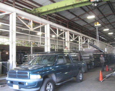 A crane loads a bundle of steel columns onto a pick-up truck.