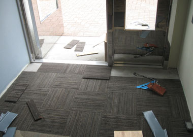 The final row of carpet squares being installed in the elevator lobby.