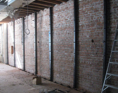 A group of steel columns installed along a brick wall.